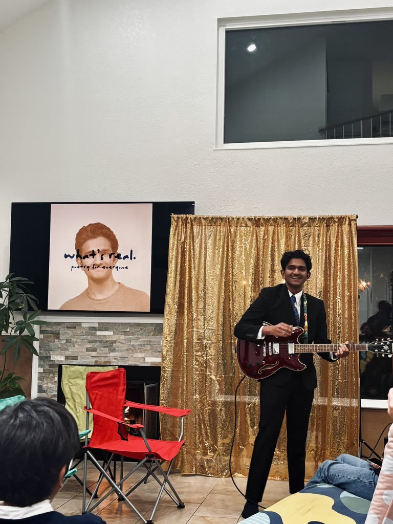 Playing guitar on a small stage at the what's real book launch, audience seated in front