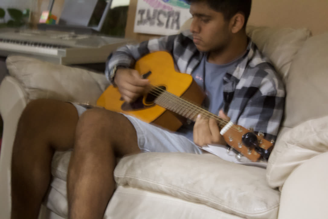 Head down, absorbed, playing acoustic guitar on a couch